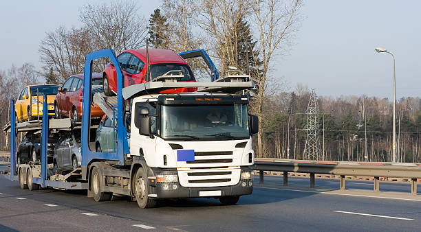 A car carrier truck transports multiple vehicles, including red, yellow, and silver cars, along a highway with trees and power lines in the background, showcasing the reliable service of AZ Car Shipping Glendale.